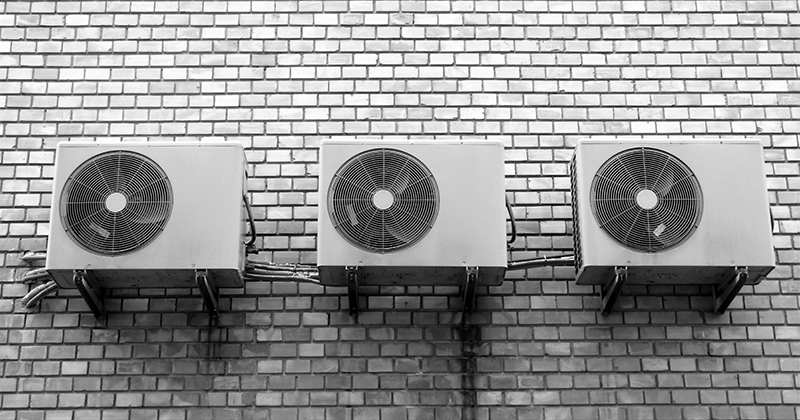 three air conditioning units on a white brick wall