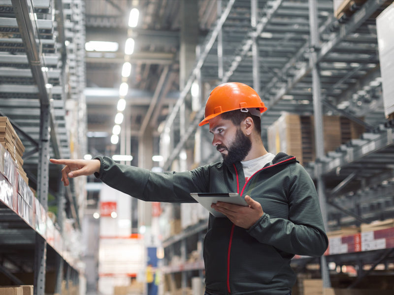 Warehouse manager checking his inventory in a large warehouse. using the tablet via the Internet is checking stock availability