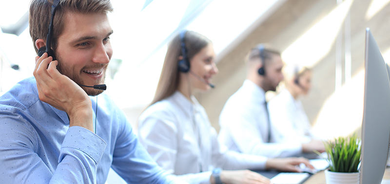 Portrait of call center worker accompanied by his team. Smiling customer support operator at work