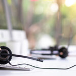 VOIP headset on desk with computer desktop at customer service and marketing support workplace. Office supplies of customer service. Communication support, call center and helpline concept.