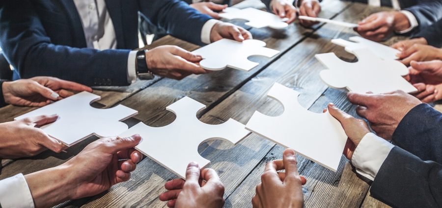 Business people and puzzle on wooden table, teamwork concept