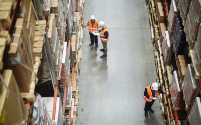 Above view of warehouse workers group in aisle between rows of tall shelves full of packed boxes and goods