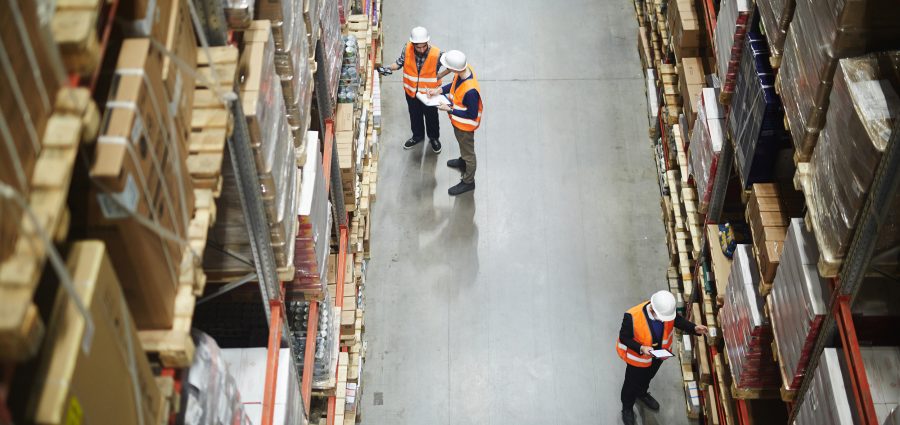 Above view of warehouse workers group in aisle between rows of tall shelves full of packed boxes and goods