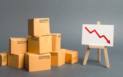 A pile of cardboard boxes and easel with red arrow down. Decrease in the quality, price, quantity and competitiveness of goods and products. Concept drop in industrial production, sales fall.