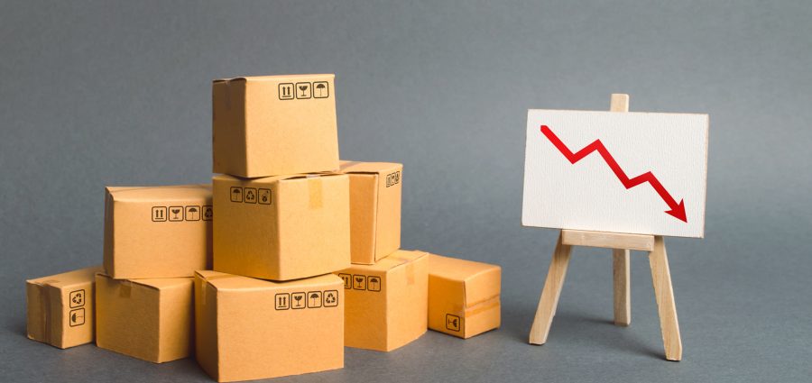 A pile of cardboard boxes and easel with red arrow down. Decrease in the quality, price, quantity and competitiveness of goods and products. Concept drop in industrial production, sales fall.