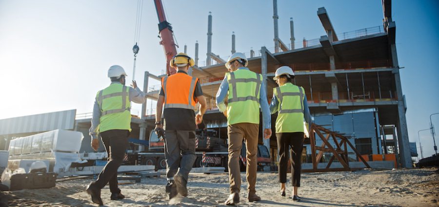 Diverse Team of Specialists Inspect Commercial, Industrial Building Construction Site. Real Estate Project with Civil Engineer, Investor and Worker. In the Background Crane, Skyscraper Formwork Frames