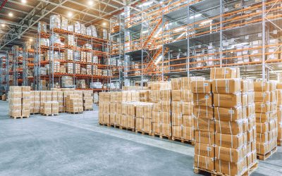 Large industrial warehouse with high racks. In the foreground are a lot of cardboard boxes.