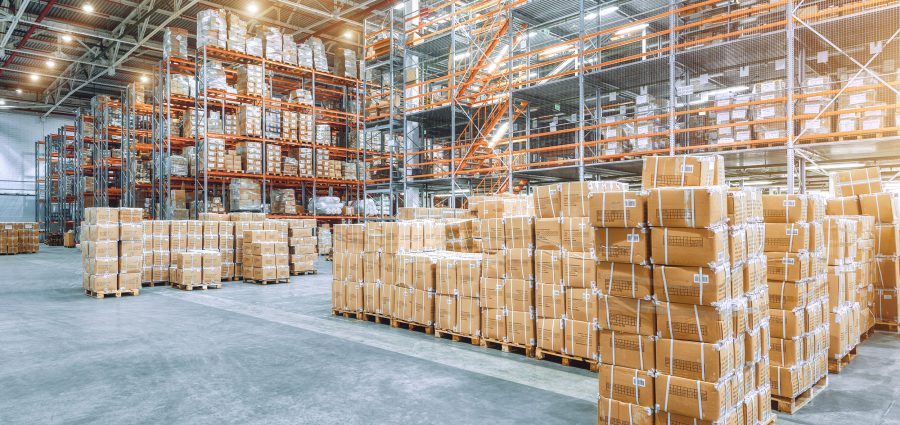 Large industrial warehouse with high racks. In the foreground are a lot of cardboard boxes.