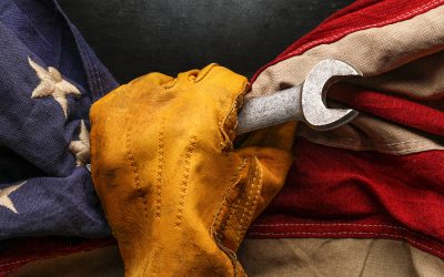 Worn work glove holding wrench tool and gripping old worn US American flag. Made in USA, American workforce, blue collar worker, or Labor Day concept.