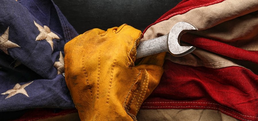 Worn work glove holding wrench tool and gripping old worn US American flag. Made in USA, American workforce, blue collar worker, or Labor Day concept.