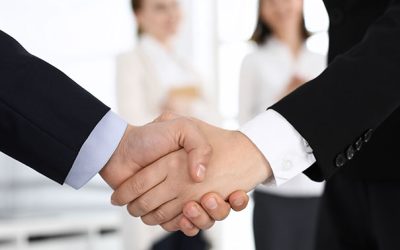 Businessman and woman shaking hands with colleagues at the background. Handshake at meeting in office. Concept of success in business.