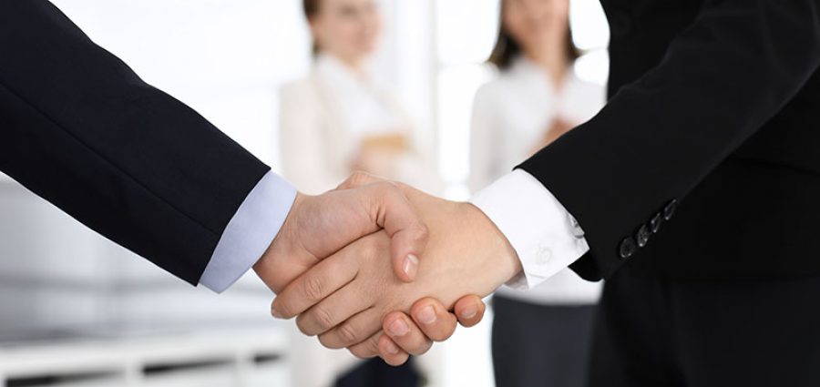 Businessman and woman shaking hands with colleagues at the background. Handshake at meeting in office. Concept of success in business.