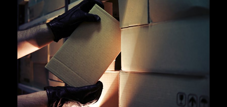 Thief hands with gloves steal a box of goods in a warehouse in the dark. Concept of problems with theft of goods and postal parcels