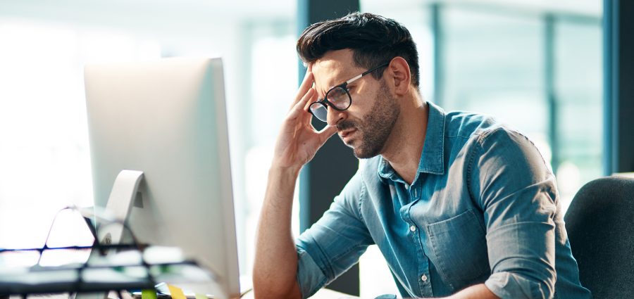 Stress, headache and frustrated business man working on computer in an office, annoyed and anxious. Male under pressure from a workload and deadline. Depressed guy experiencing burnout at work.