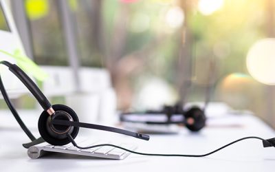 VOIP headset on desk with computer desktop at customer service and marketing support workplace. Office supplies of customer service. Communication support, call center and helpline concept.