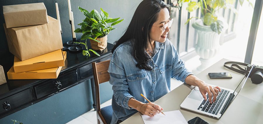 Young business woman working online e-commerce shopping at her shop. Young woman seller prepare parcel box of product for deliver to customer. Online selling, e-commerce.