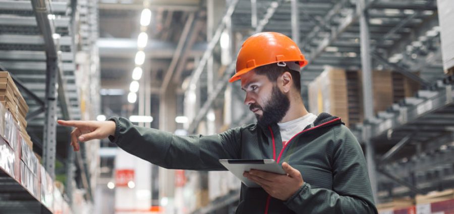 Warehouse manager checking his inventory in a large warehouse. using the tablet via the Internet is checking stock availability