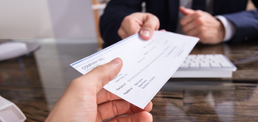 Close-up Of A Businessperson's Hand Giving Cheque To Colleague At Workplace