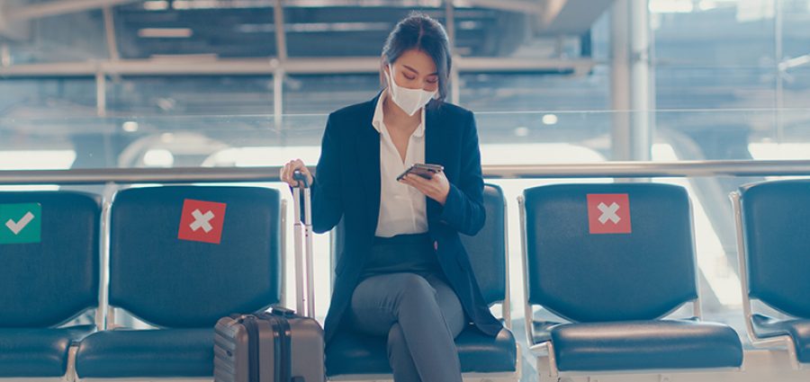 business lady traveller wear suit sitting with suitcase and use smart phone chat message in bench wait for flight at airport. Business travel commuter in covid pandemic, Business travel concept.