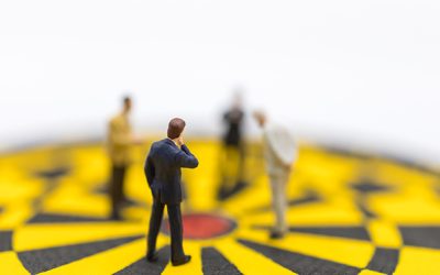 Business, Planning, Succession and Management Concept. Close up of group of businessman miniature figure standing and looking to center of yellow and black dart board on white background.