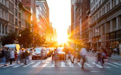 Crowds of busy people walking through the intersection of 5th Avenue and 23rd Street in Manhattan, New York City with bright sunset background