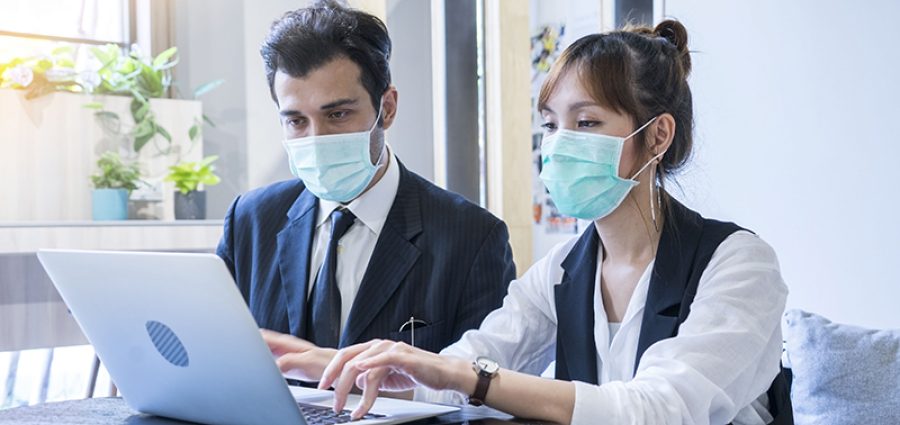 man and woman wearing masks working on a laptop together